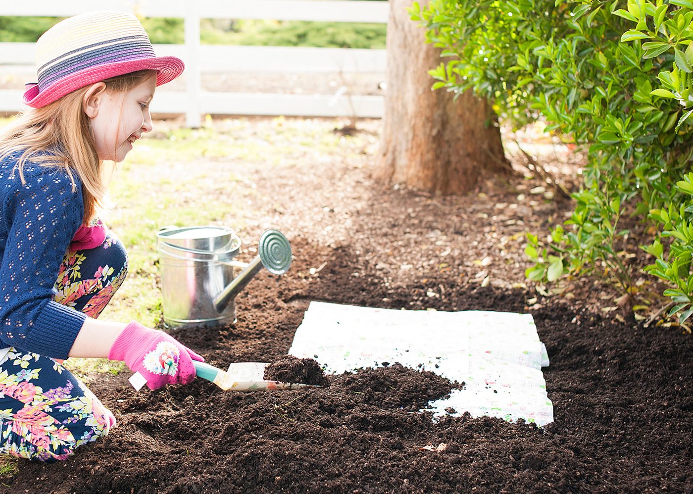 Child laying a seed mat on garden soil